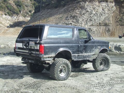 1978 Ford Bronco - This lifted Ford Bronco is parked off-road in a dirt lot with hills in the background.