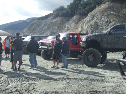 1978 Ford Bronco - A group of people stand around modified trucks and SUVs in a dry, hilly area.