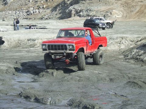 1978 Ford Bronco - A modified red pickup truck navigates a muddy off-road course with other vehicles present.