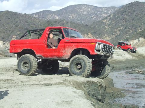 1978 Ford Bronco - A lifted red 1978 Ford Bronco navigates a rocky off-road course with a second vehicle visible in the distance.