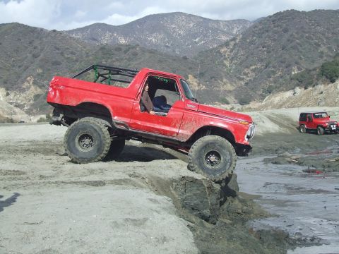 1978 Ford Bronco - A red 1978 Ford Bronco navigates a challenging off-road terrain with another red Jeep in the background.