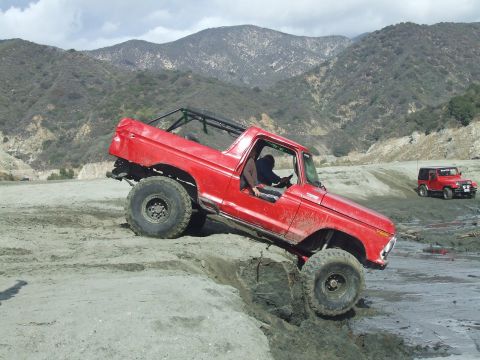 1978 Ford Bronco - A red 1978 Ford Bronco tackles a challenging off-road course with another vehicle visible in the background.