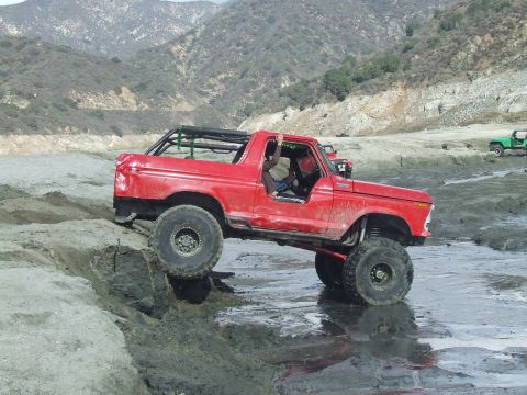 1978 Ford Bronco - A red 1978 Ford Bronco navigates a muddy off-road course with a driver visible inside.