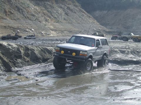 1978 Ford Bronco - A lifted silver SUV navigates a muddy terrain, with other vehicles visible in the background.