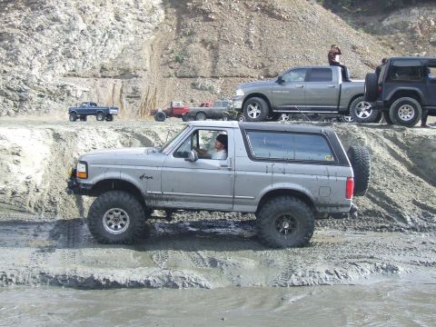 1978 Ford Bronco - Modified Ford Bronco navigates a muddy off-road course with other vehicles present.