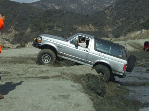 1978 Ford Bronco - A silver SUV navigates a challenging muddy terrain, with another red SUV visible in the background.