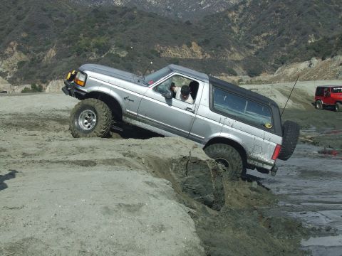 1978 Ford Bronco - A silver SUV navigates a challenging dirt terrain, with another vehicle visible in the distance.