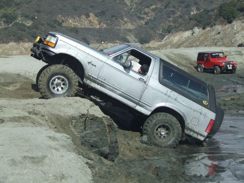1978 Ford Bronco - A silver Ford Bronco navigates a challenging off-road terrain, while a red Jeep waits behind.