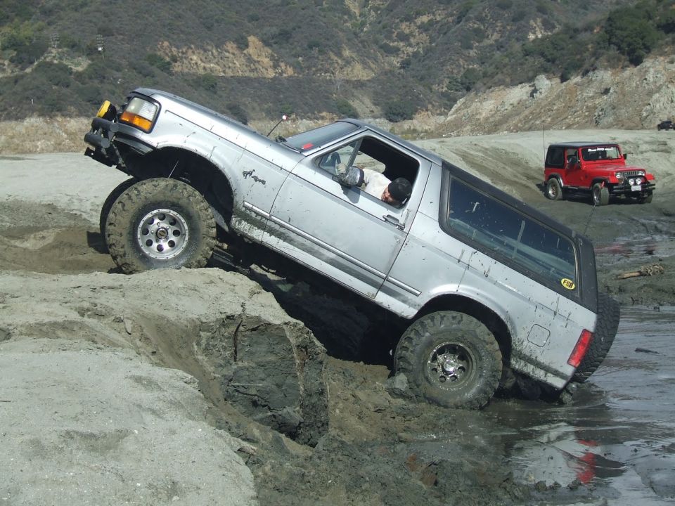 Silver Ford Bronco climbing a dirt hill with a red Jeep in the background