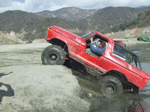 1978 Ford Bronco - A red 1978 Ford Bronco navigates a challenging muddy terrain, its off-road capabilities.