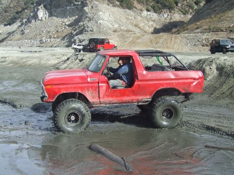 1978 Ford Bronco - A red 1978 Ford Bronco navigates a muddy terrain with other off-road vehicles in the background.