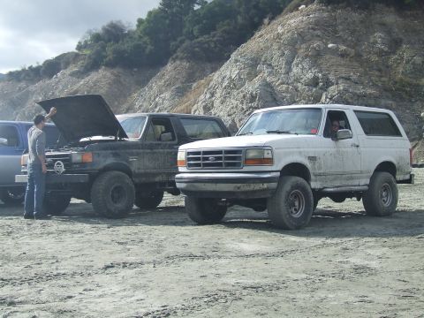 1978 Ford Bronco - Two Ford Broncos are parked on a dirt lot with a rocky hillside in the background.
