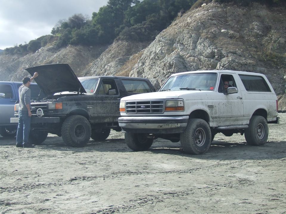 Two Ford Broncos parked on dirt, one with hood up