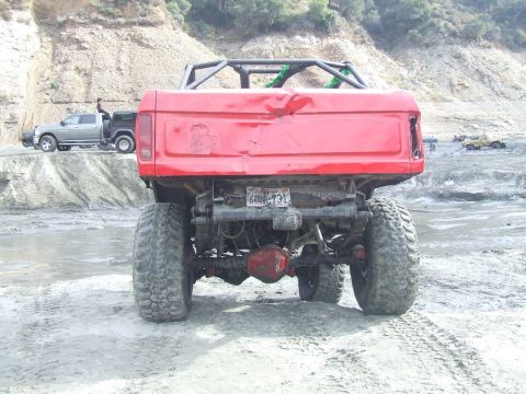 1978 Ford Bronco - A red 1978 Ford Bronco with a roll cage is seen from the rear, with another truck in the background.