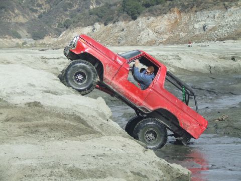 1978 Ford Bronco - A red off-road truck navigates a challenging dirt and water obstacle course.