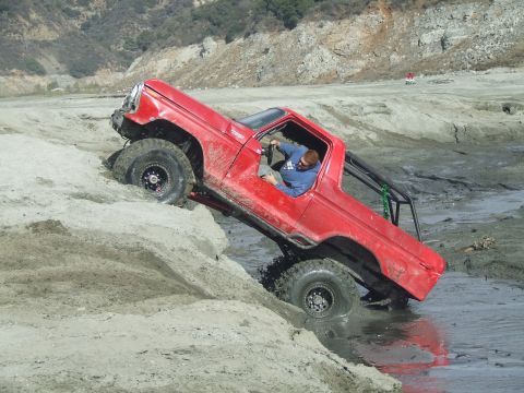 1978 Ford Bronco - A red off-road truck navigates a challenging muddy terrain, with its driver actively engaged.