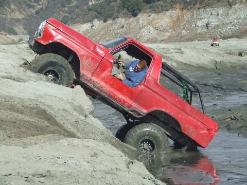 1978 Ford Bronco - A red 1978 Ford Bronco struggles for traction while navigating a steep, muddy embankment.