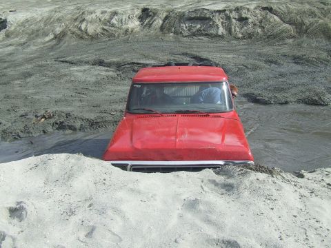 1978 Ford Bronco - A red truck is stuck in a muddy area, with its front end partially submerged in water and sand.