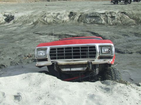1978 Ford Bronco - A red 1978 Ford Bronco navigates a muddy terrain, its front grille prominently visible.