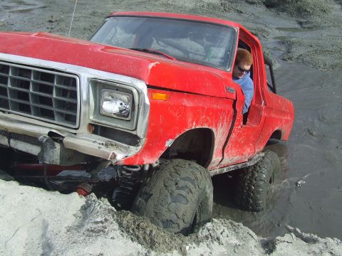 1978 Ford Bronco - Red 1978 Ford Bronco is stuck deep in mud with its front tires submerged.