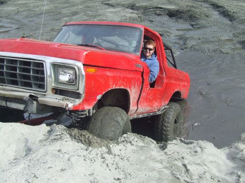1978 Ford Bronco - A red 1978 Ford Bronco navigates a muddy terrain, with its driver visible and smiling.