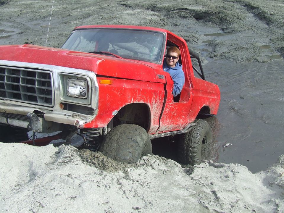 Red 1978 Ford Bronco stuck in mud with driver smiling
