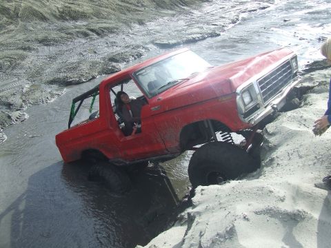 1978 Ford Bronco - A red 1978 Ford Bronco is stuck in mud and sand, with its front tire partially submerged.