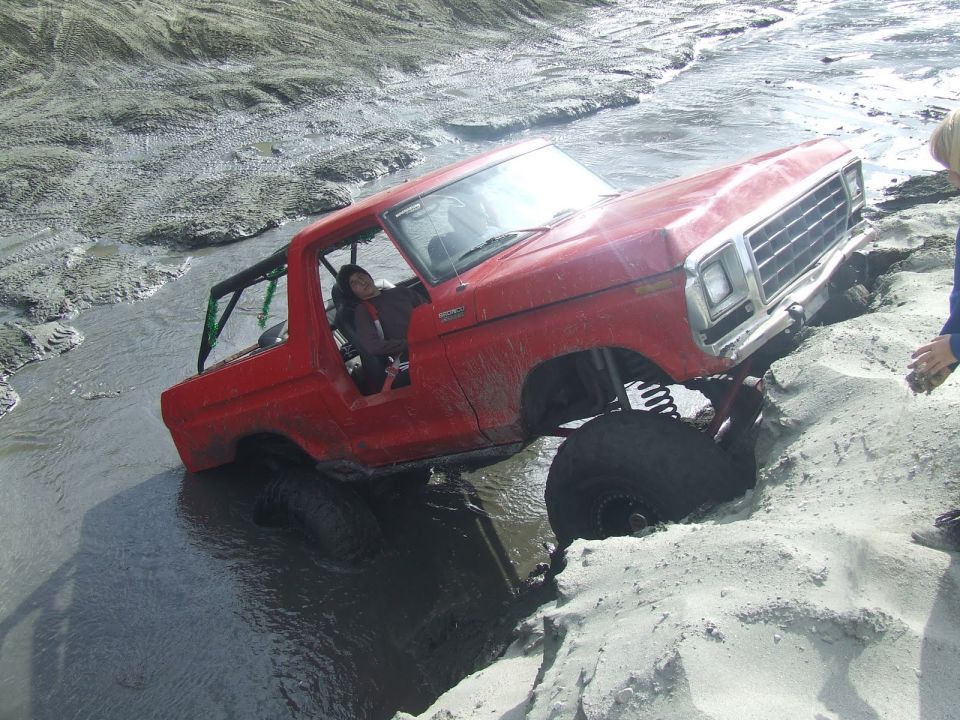 Red 1978 Ford Bronco stuck in mud with a roll cage, viewed from the front-right