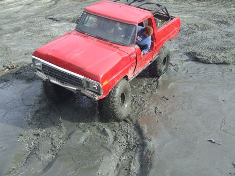 1978 Ford Bronco - A red 1978 Ford Bronco navigates a muddy terrain, with a driver visible inside.