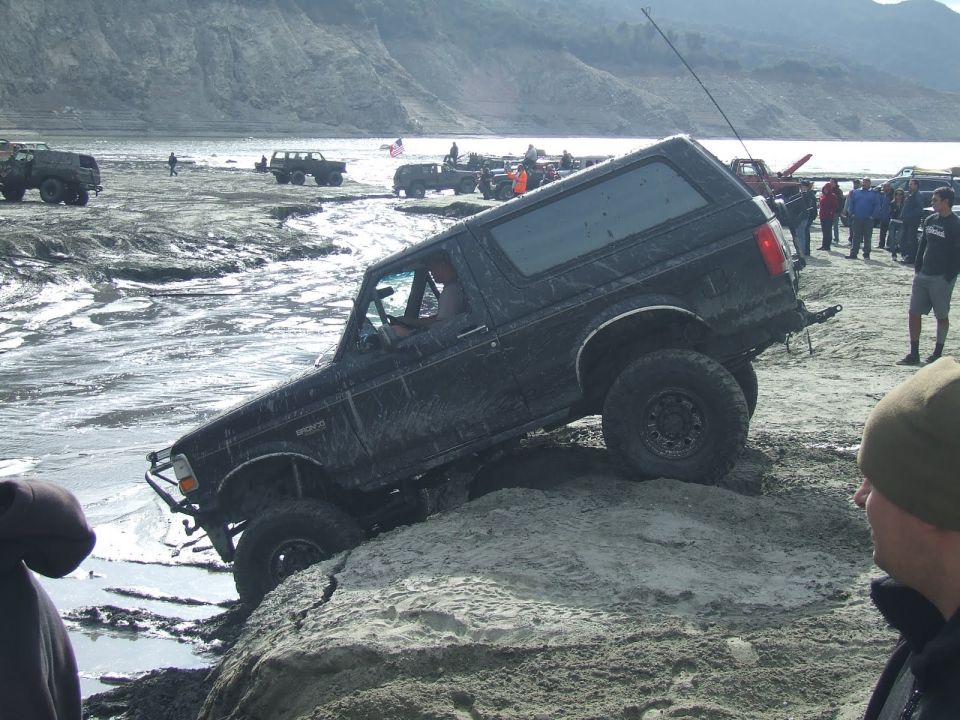Black Ford Bronco attempting rocky incline with other vehicles and people in background