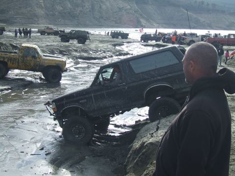 1978 Ford Bronco - Several off-road vehicles navigate a muddy terrain, with one Bronco prominently featured.