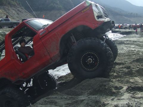 1978 Ford Bronco - A red off-road vehicle is shown in a challenging outdoor environment with other vehicles in the background.