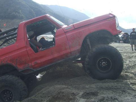 1978 Ford Bronco - This red 1978 Ford Bronco is navigating a sandy terrain with its large off-road tires.