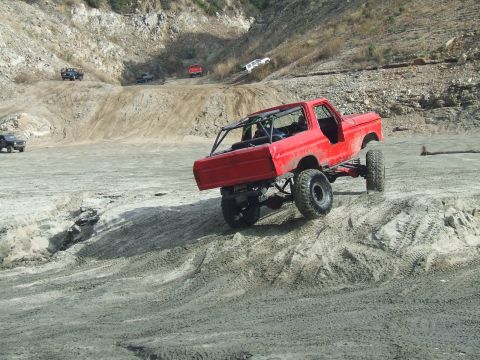 1978 Ford Bronco - A red 1978 Ford Bronco navigates a challenging dirt terrain with other vehicles visible in the background.