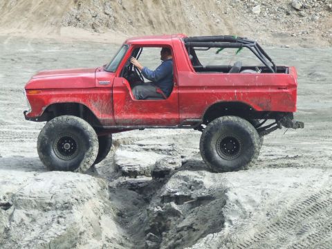 1978 Ford Bronco - A red 1978 Ford Bronco navigates a challenging off-road course with large tires.