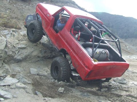 1978 Ford Bronco - A heavily modified red off-road vehicle navigates a steep, rocky incline with a second vehicle visible in the background.