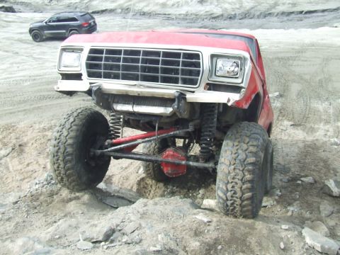 1978 Ford Bronco - A red 1978 Ford Bronco is shown with a prominent grille and lifted suspension, navigating rough terrain.