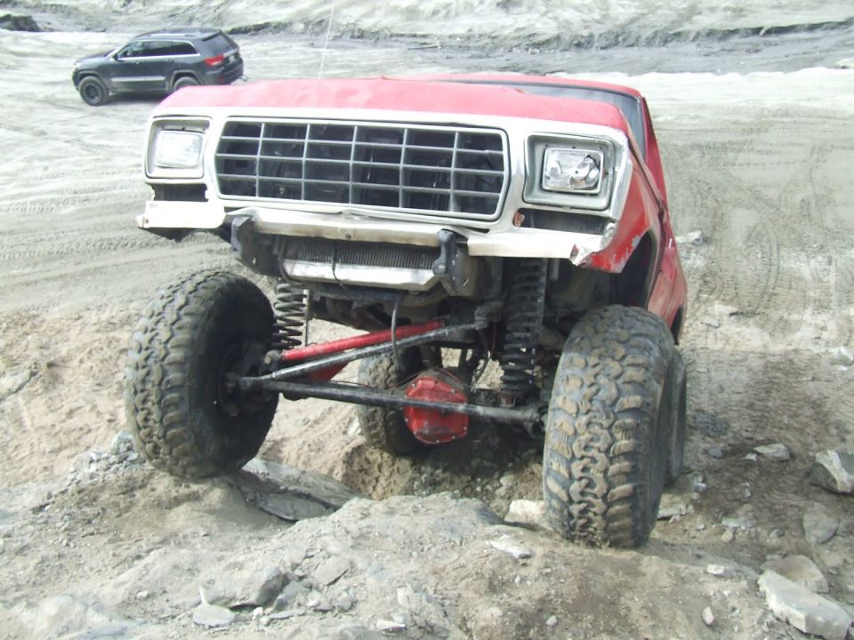 Red 1978 Ford Bronco with large tires and lifted suspension on rocky terrain