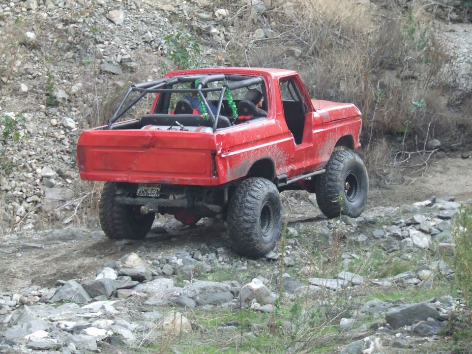 Red 1978 Ford Bronco with roll cage on rocky terrain