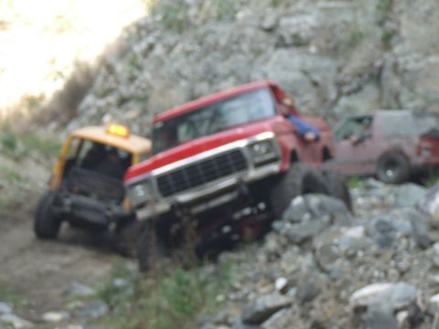 1978 Ford Bronco - Multiple off-road vehicles are seen navigating a challenging, rocky incline.