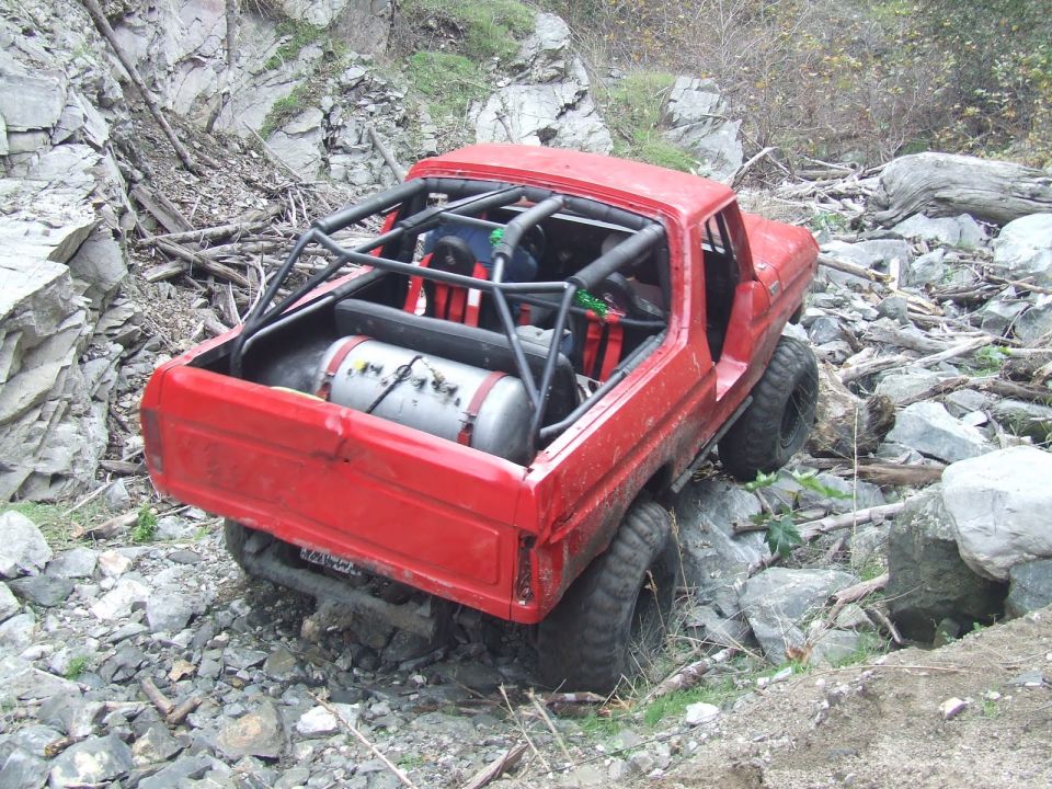 Red 1978 Ford Bronco with roll cage and external tank navigating rocky terrain