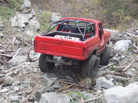 1978 Ford Bronco - This red 1978 Ford Bronco navigates a challenging rocky trail, equipped with a prominent roll cage for off-road safety.