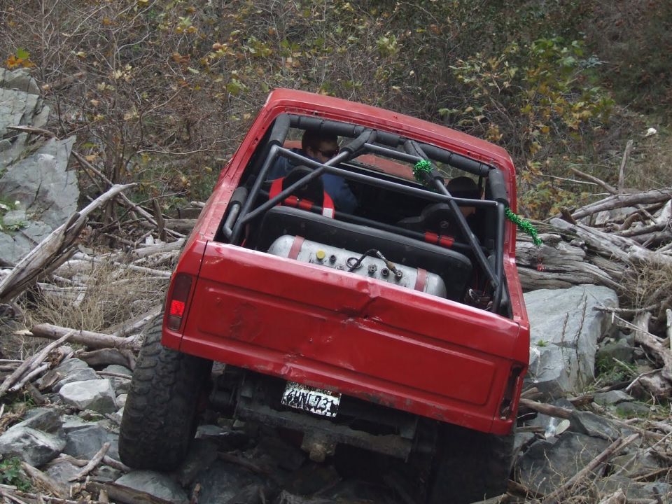 Red SUV with roll cage and external tank navigating rocky terrain