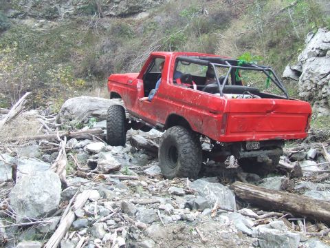1978 Ford Bronco - A red 1978 Ford Bronco is shown off-roading on a rocky, debris-filled path.