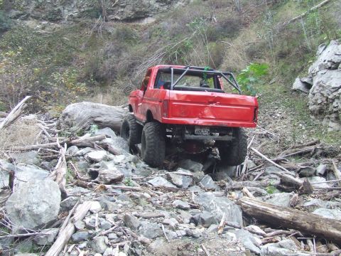 1978 Ford Bronco - A heavily modified red truck navigates a challenging, rocky off-road path.