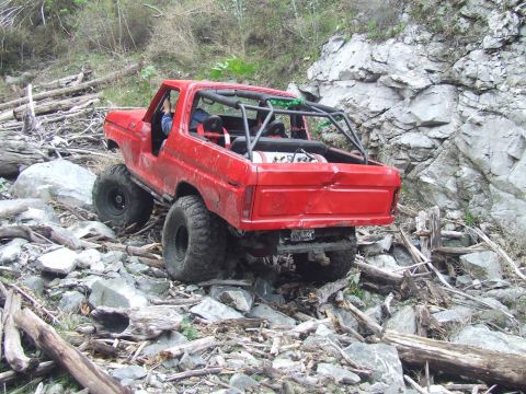 1978 Ford Bronco - A red 1978 Ford Bronco is shown off-roading over rocks and logs.