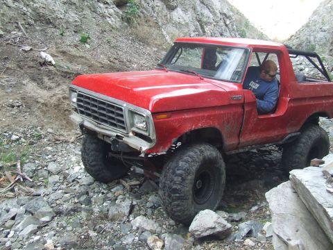 1978 Ford Bronco - A red 1978 Ford Bronco is shown off-roading on a rocky, uneven terrain.