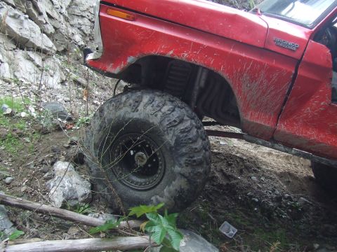 1978 Ford Bronco - A red 1978 Ford Bronco navigates challenging rocky terrain, its large off-road tires gripping the ground.