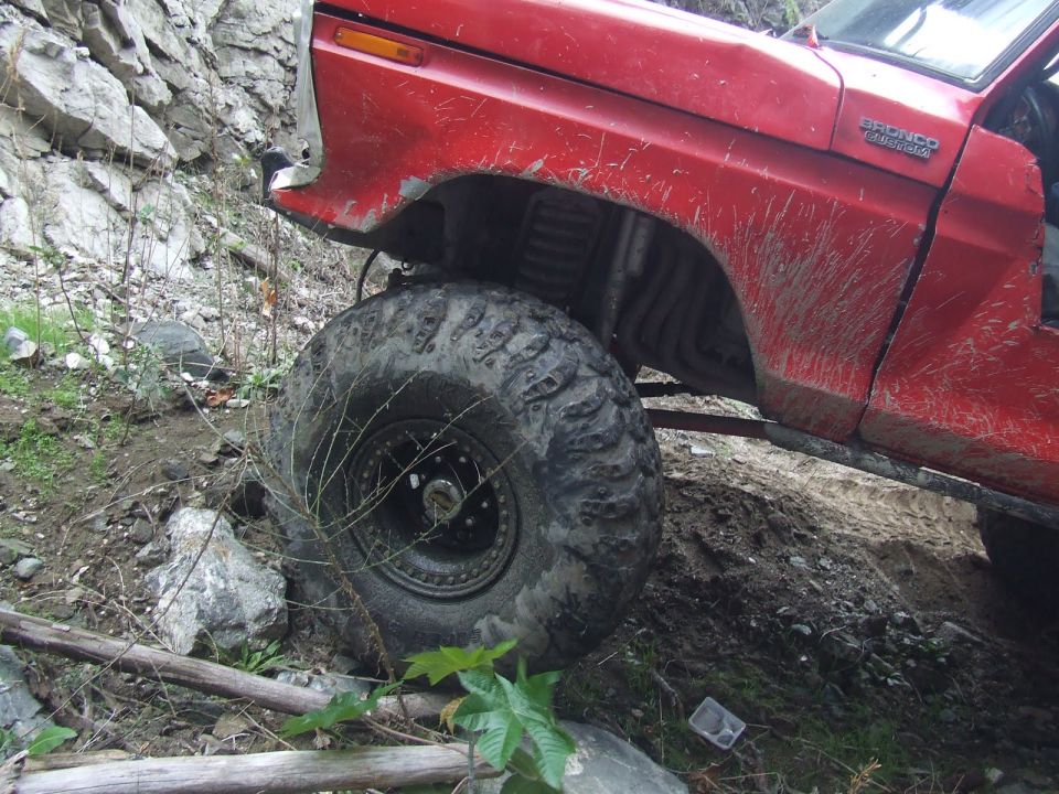 Red 1978 Ford Bronco with large off-road tires on rocky terrain