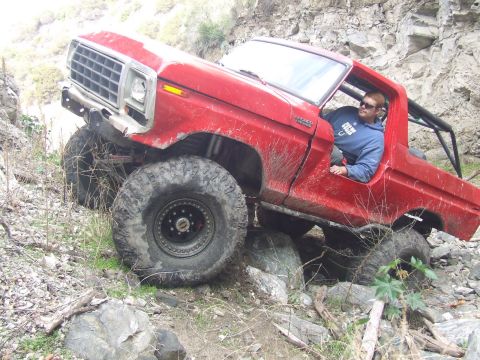 1978 Ford Bronco - A red 1978 Ford Bronco navigates a rocky, off-road trail with its tires angled over boulders.